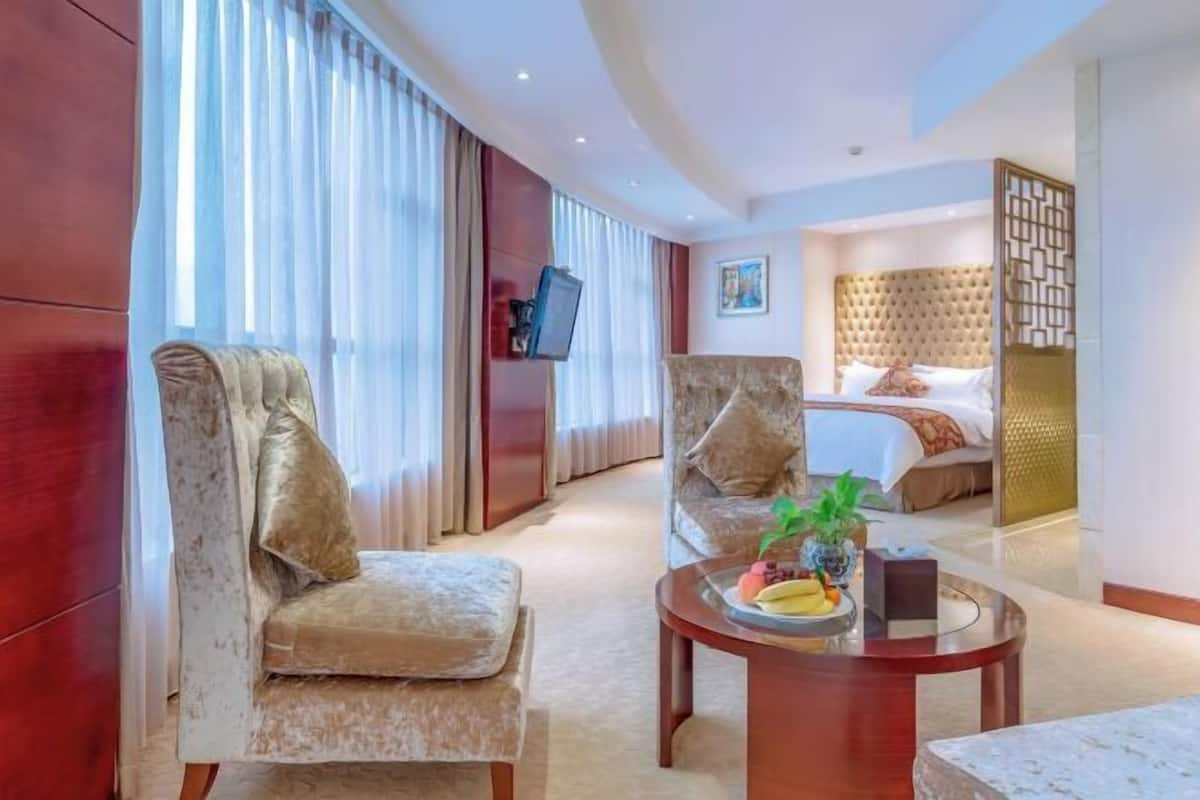 A hotel room with a large bed, two armchairs, a coffee table with fruit, and a TV on a stand.