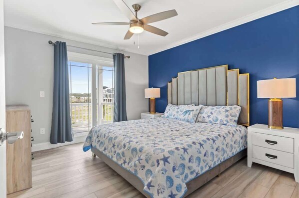 Une chambre à coucher avec un lit, deux tables de chevet, un ventilateur de plafond et une vue par la fenêtre.