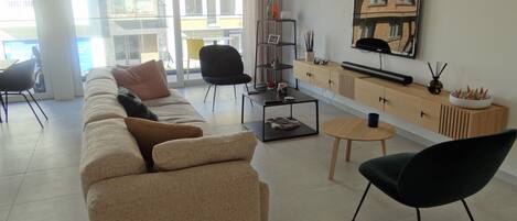 Una sala de estar moderna con un sofá color beige, un sillón negro, una mesa de centro y un televisor montado en la pared.