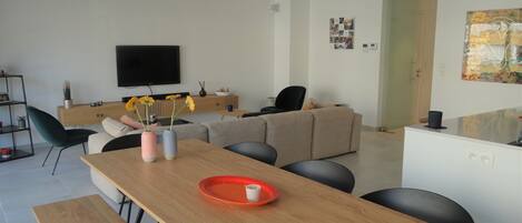 Uma sala de estar moderna com uma mesa de jantar de madeira, um sofá e uma televisão na parede.