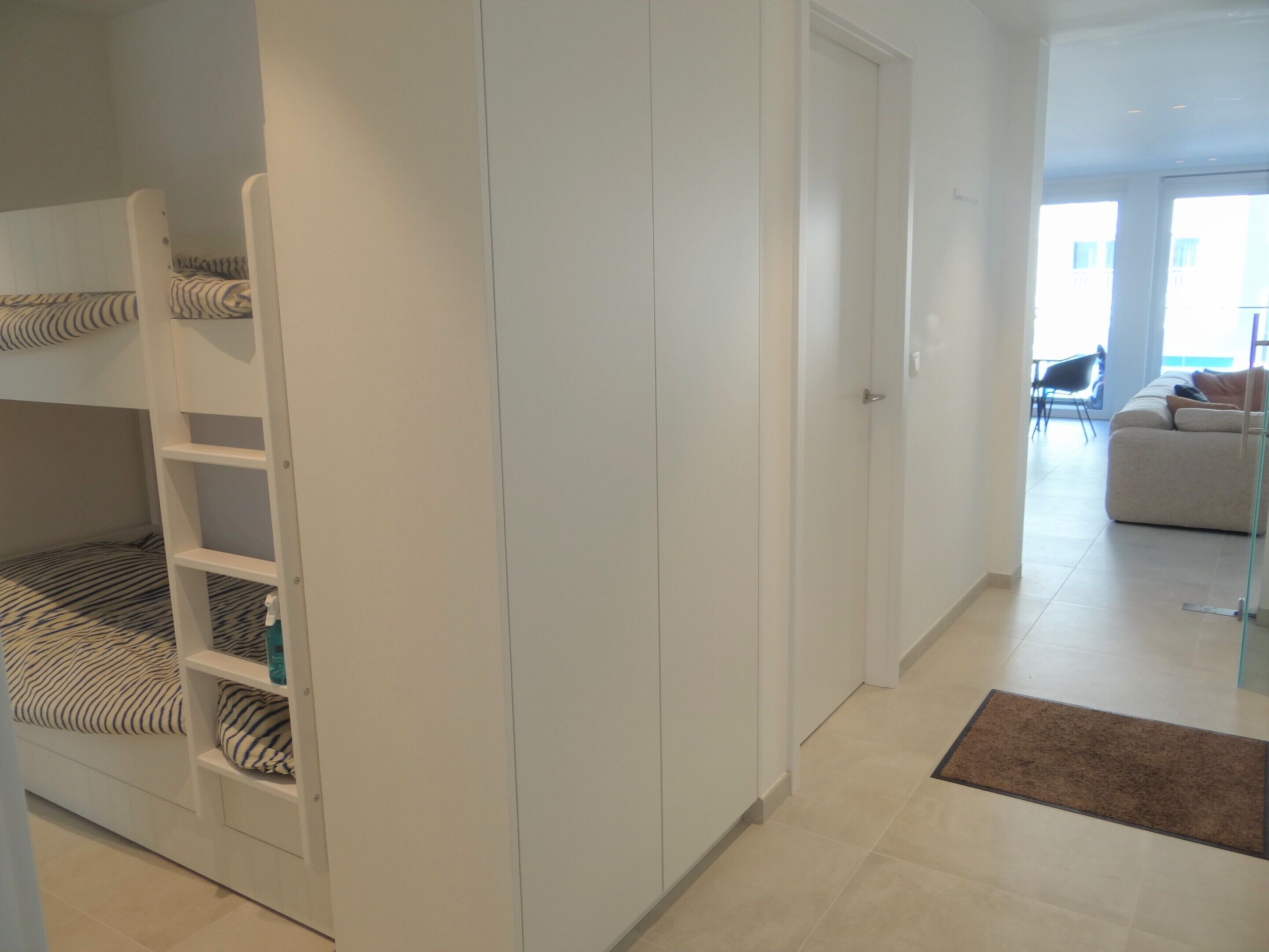 Une chambre avec un lit superposé, une armoire, un canapé et une porte vitrée donnant sur un balcon.