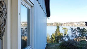 Una casa con ventana que da a un lago y una vista distante de un puente.