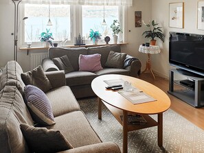 A living room with a sectional sofa, a coffee table, a TV, and a window with plants. - 5 Person Holiday Home in Uddevalla (Uddevalla)
