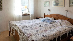 Un dormitorio con cama de madera, cubrecama de encaje y ventana con cortinas.
