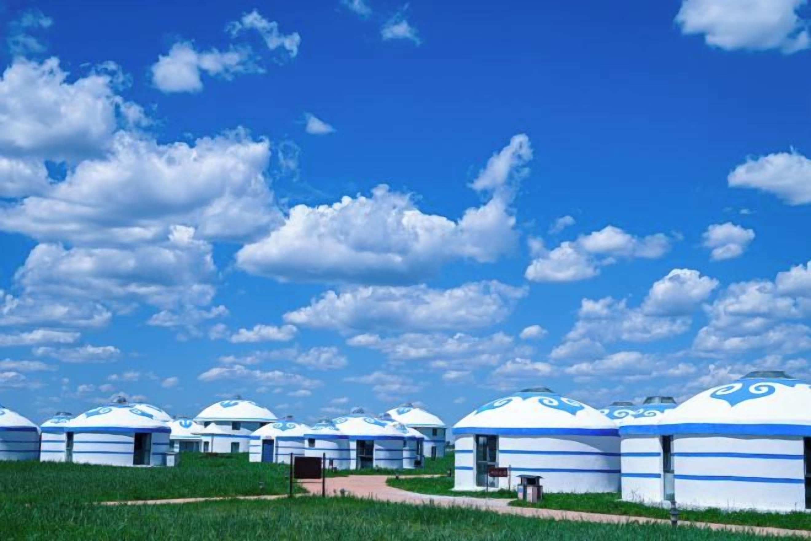 A row of traditional blue and white yurts with a clear sky and clouds in the background.