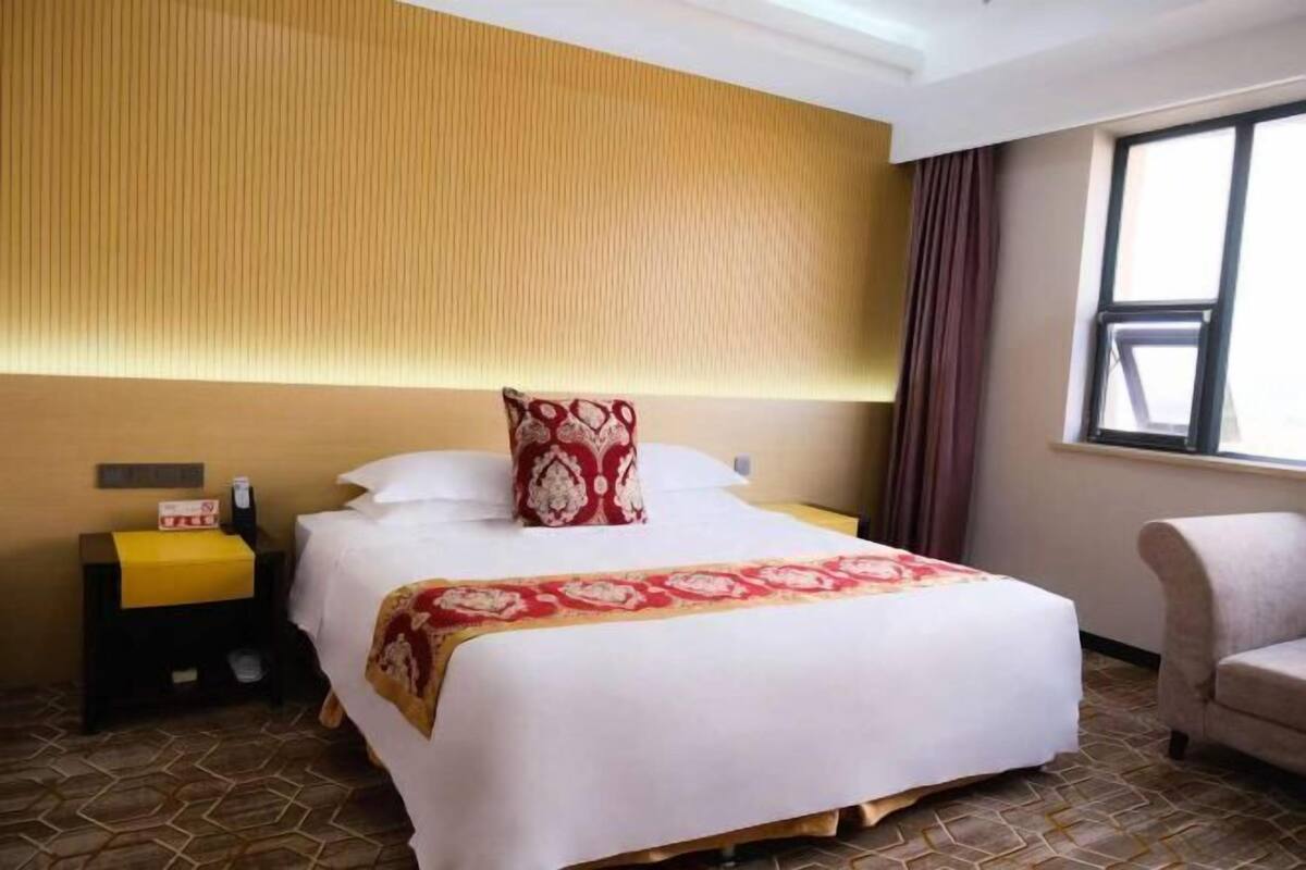 Habitación de hotel con una cama grande, una mesita de noche, una silla y un ventanal con cortinas.