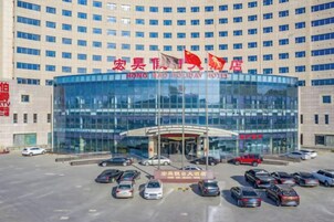 A multi-story hotel building with a glass facade, multiple flags, and a parking lot with several cars.
