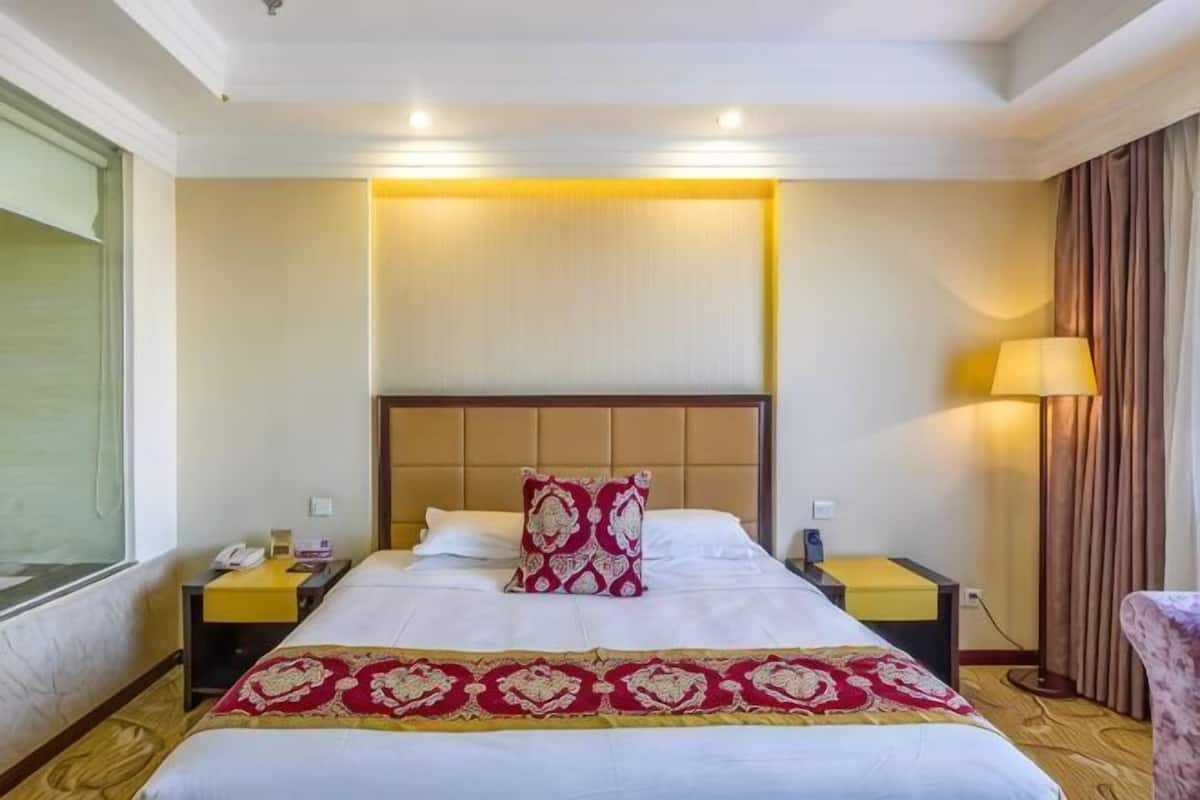 Una habitación de hotel con una cama grande, mesitas de noche, una lámpara y un ventanal.