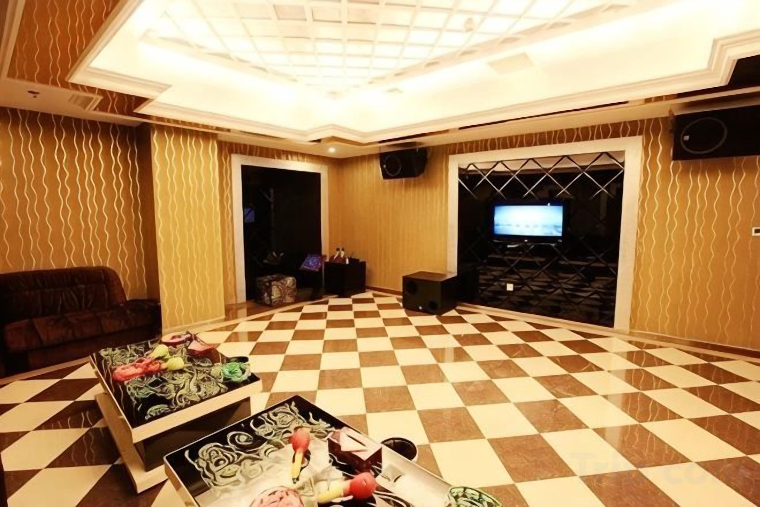 Una habitación amplia con piso a cuadros, un sofá, una mesa de centro con objetos y un televisor.