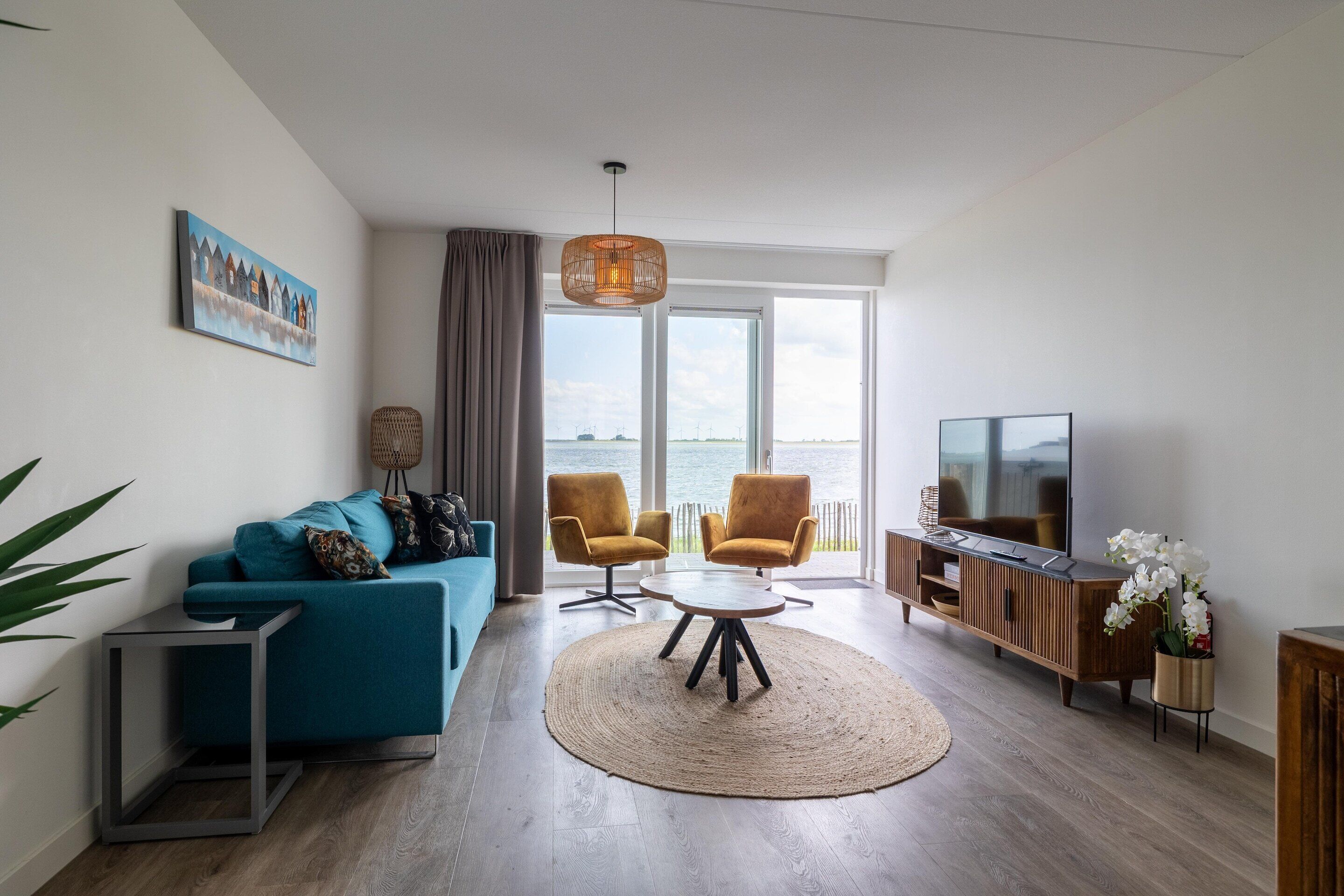 Un salon moderne comprenant un canapé, deux fauteuils, une table basse, un téléviseur et une grande fenêtre donnant sur un beau paysage.