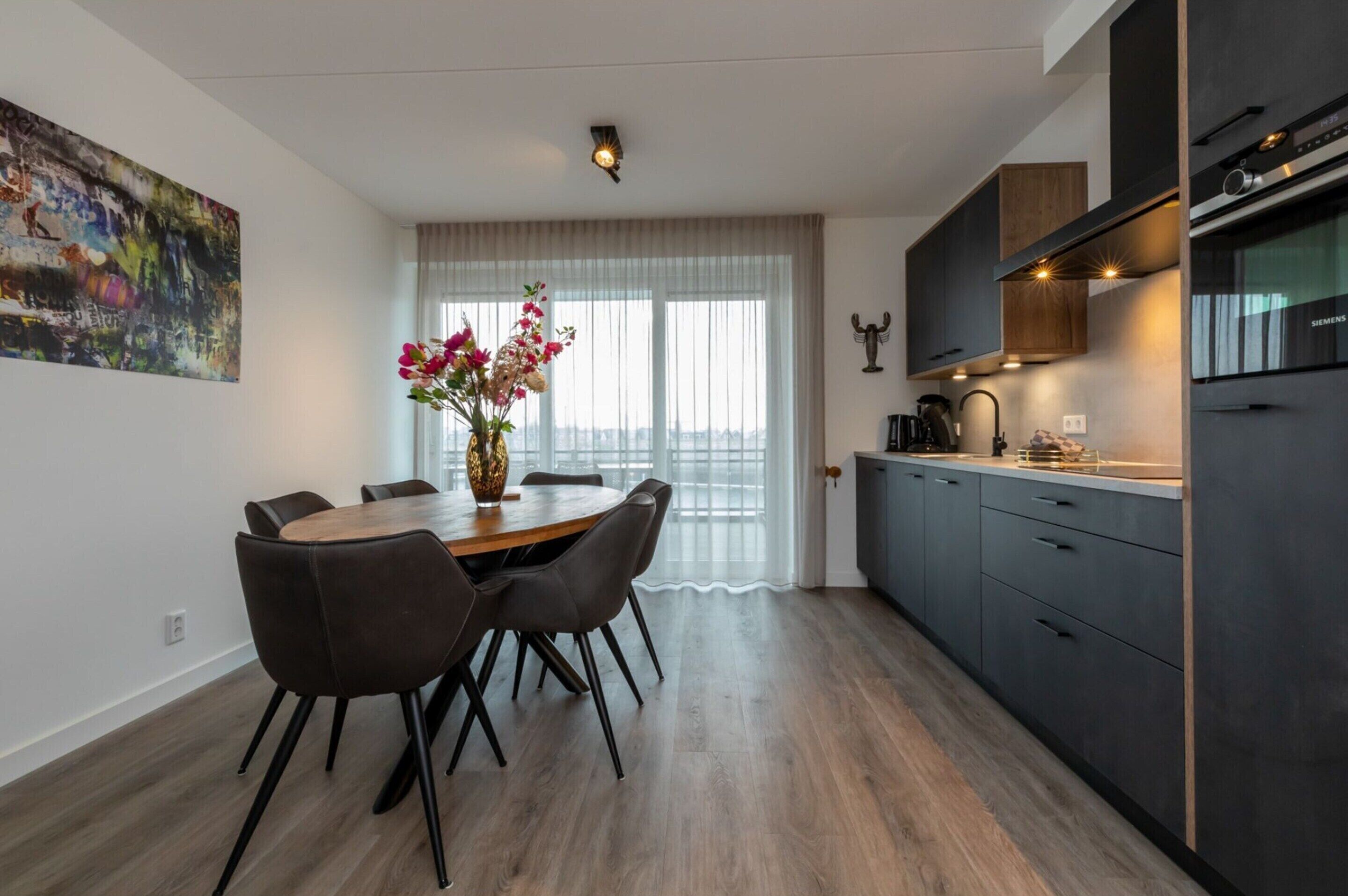 Una cucina moderna con mobili scuri, forno integrato e zona pranzo con tavolo e sedie in legno.