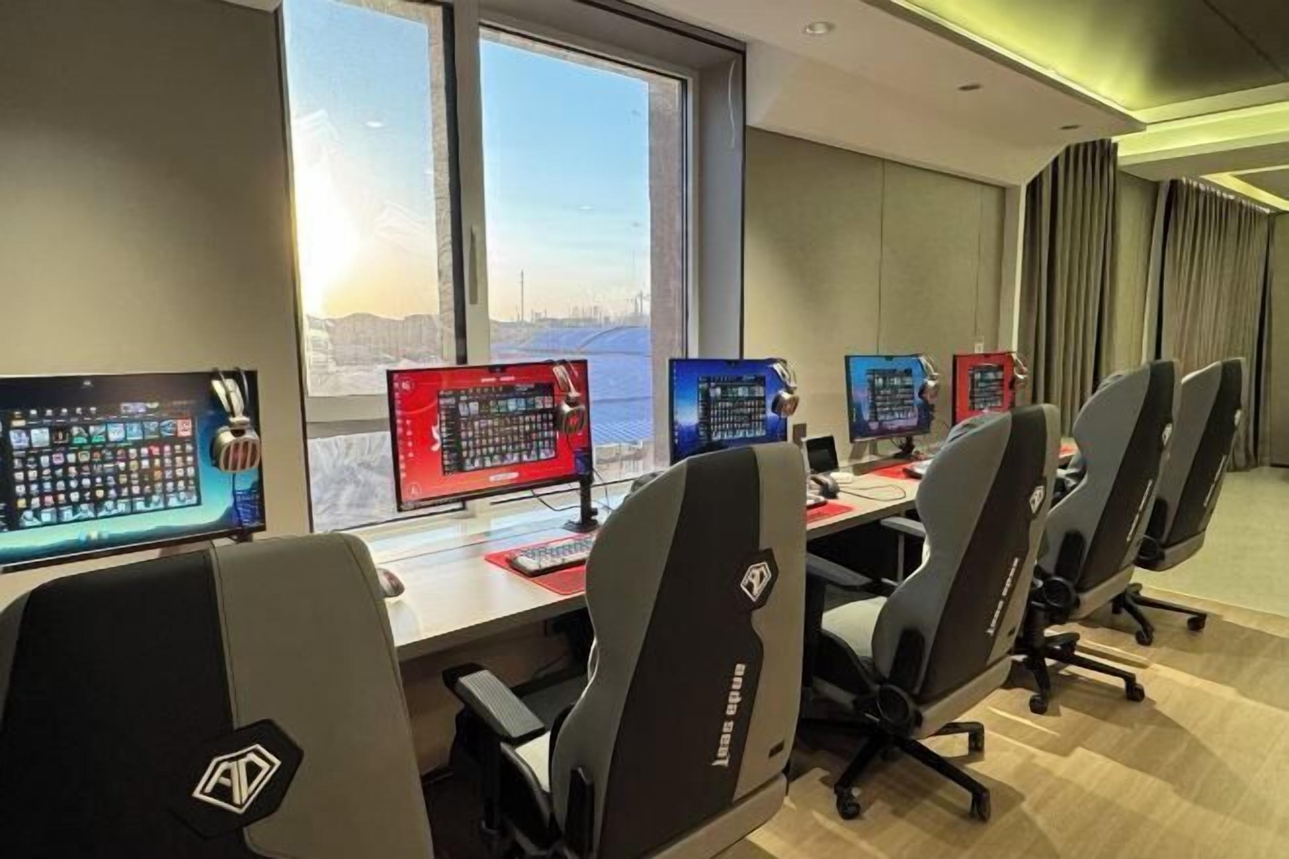 Ein Konferenzraum mit mehreren Monitoren, Gaming-Stühlen und Blick auf die Stadt.
