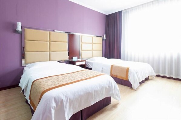 Habitación de hotel con dos camas, un cabecero grande y una ventana con cortinas.
