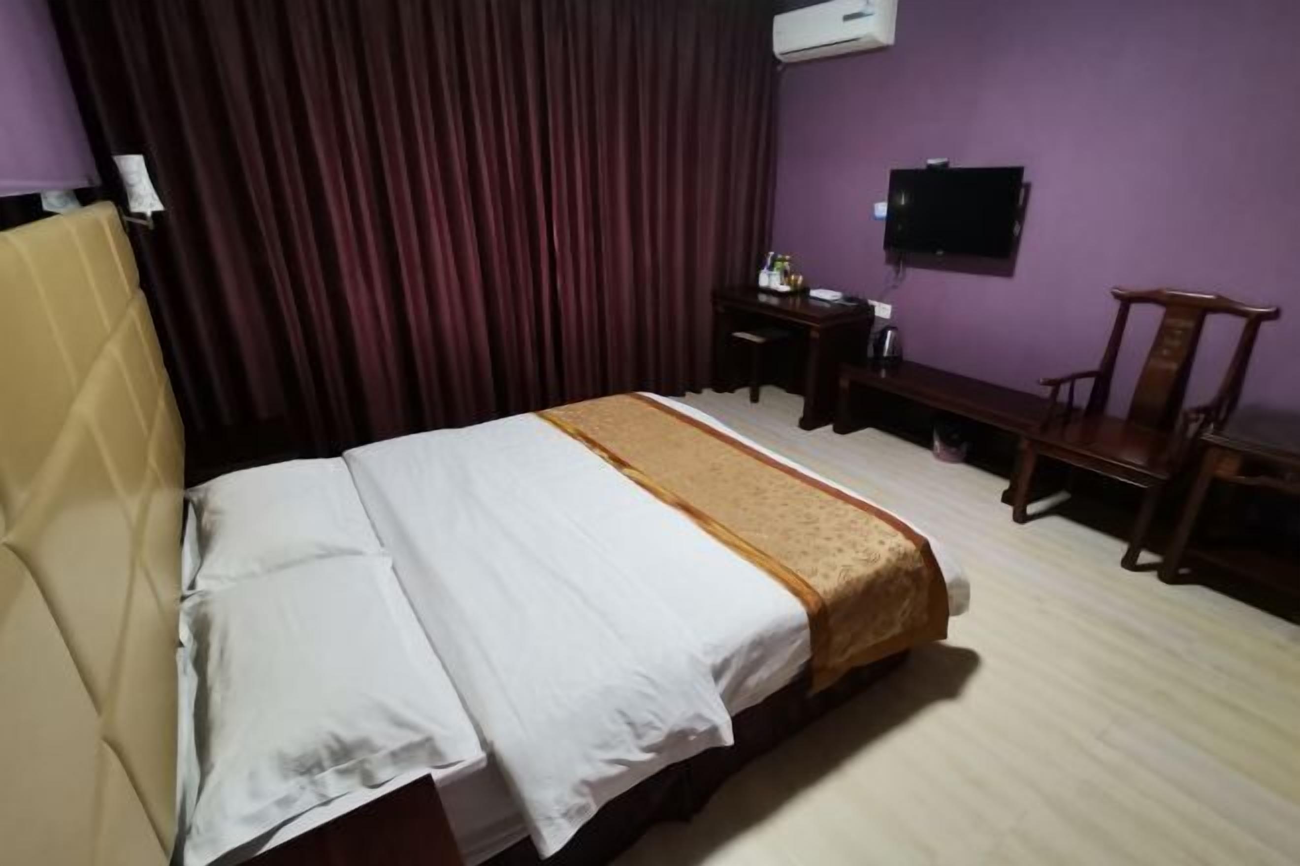 Una habitación de hotel con cama, escritorio, silla, televisor y aire acondicionado.