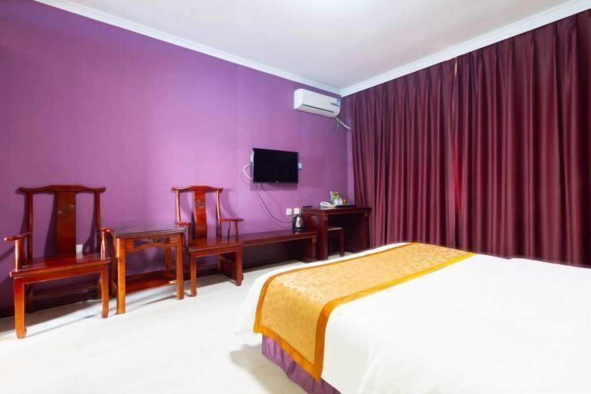 A hotel room with a bed, a desk, a chair, a television, and an air conditioning unit.