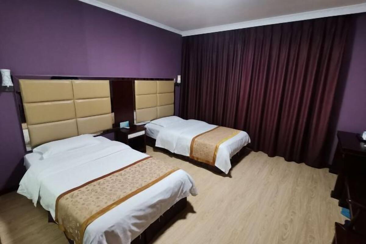 A hotel room with two beds, a wooden floor, and purple walls.