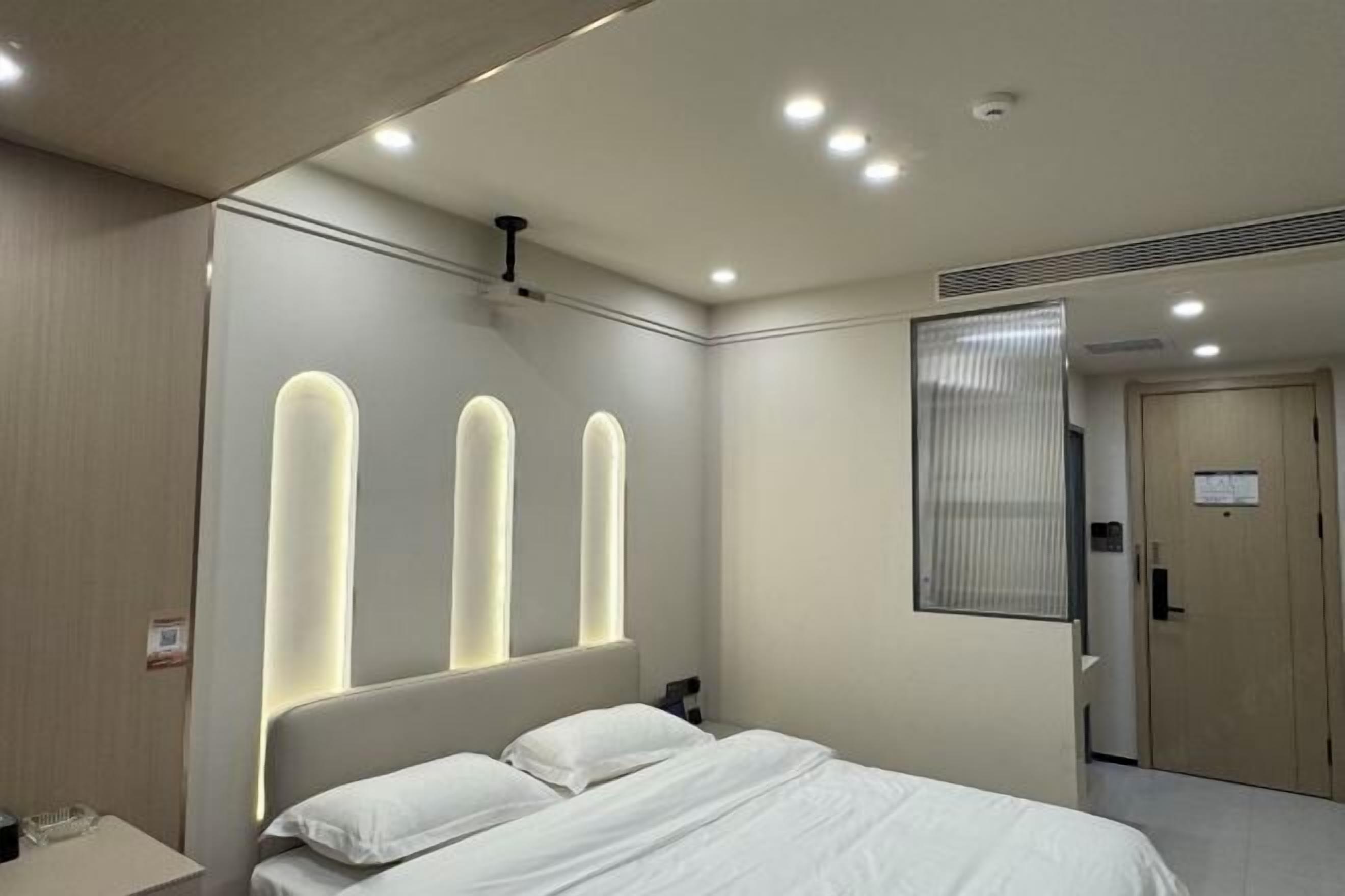 A modern hotel room with a bed, bedside table, and a wall-mounted light fixture.