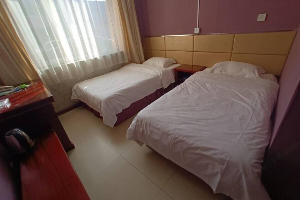 A hotel room with two single beds, a wooden desk, and a window with curtains.