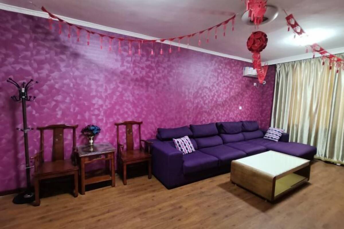 A living room with a purple sofa, a wooden coffee table, and a coat rack.