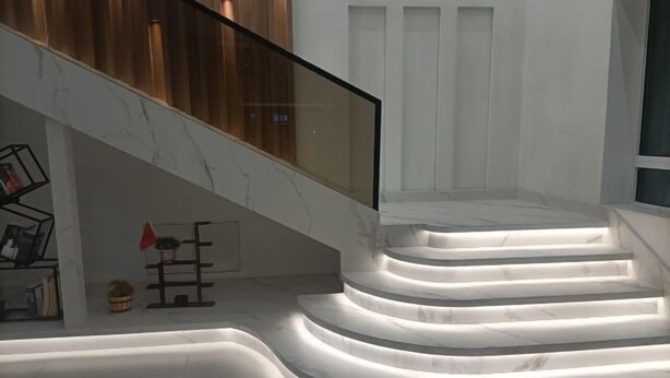 Uma escadaria de mármore com corrimão de vidro que dá para um patamar.