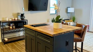 A modern kitchen with a wooden ceiling, a built-in island with black cabinets, and a flat-screen TV mounted on the wall. - 1BR Modern Bungalow close to Fishing, Navy Base and Ocean (Jacksonville)