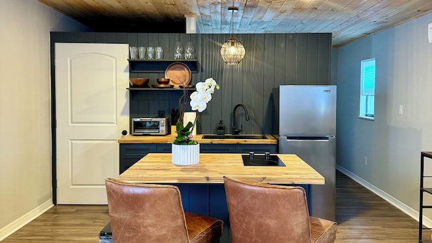 A modern kitchen with a wooden ceiling, a central island, and two leather chairs. - 1BR Modern Bungalow close to Fishing, Navy Base and Ocean (Jacksonville)