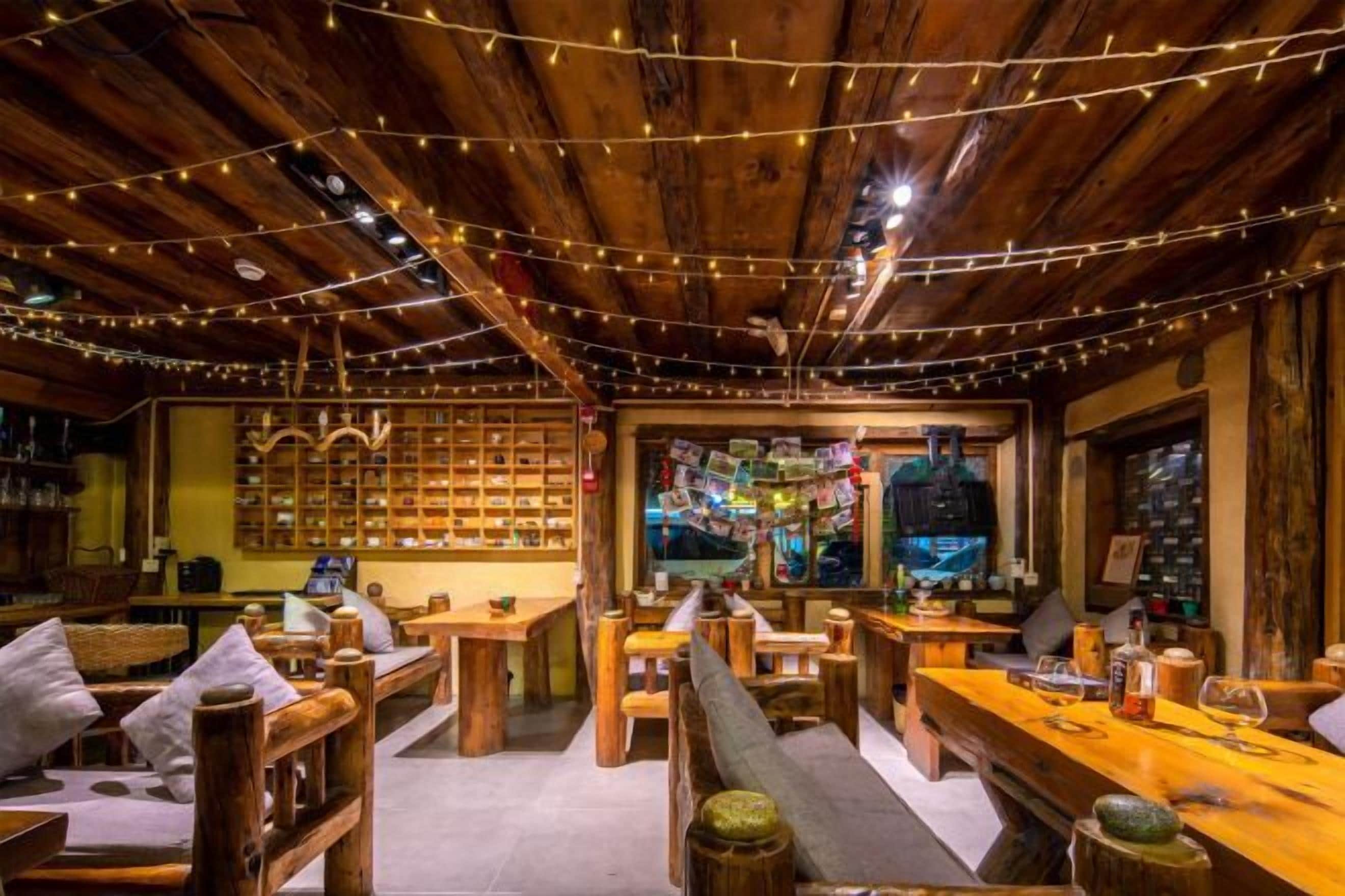 A cozy wooden interior with string lights, wooden furniture, and a bar area.