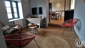A modern living room with a flat-screen TV, wicker chairs, a dining area, and a kitchen in the background. - Gîte "domaine Gilles Coperet" (REGNIE DURETTE)