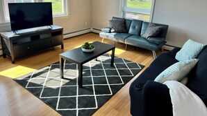 Ein Wohnzimmer mit Fernseher, Sofa, Couchtisch und Teppich.