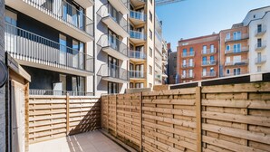 Ein moderner Wohnkomplex in der Stadt mit mehreren Balkonen, einem Holzzaun und einer gefliesten Terrasse.