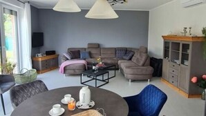 A modern living room with a grey sofa set, a dining table with chairs, and hanging pendant lights. - Garden Magic Comfortable Holiday Residence (Goch)
