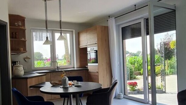 A modern kitchen with a dining area, large windows, and a sliding glass door leading to a garden. - Garden Magic Comfortable Holiday Residence (Goch)