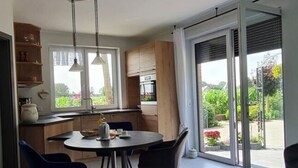 Une cuisine moderne avec un coin repas, de grandes fenĂŞtres et une porte-fenĂŞtre coulissante donnant sur un jardin.