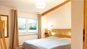 A bedroom with a wooden bed frame, a window with curtains, a bedside lamp, and a wooden floor. - Holiday Apartment Tannenhof Bornholdt (Lutzhorn)