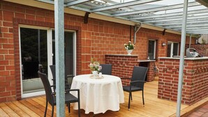 A covered patio with a table and chairs, a brick wall, and a grill area. - Holiday Apartment Tannenhof Bornholdt (Lutzhorn)