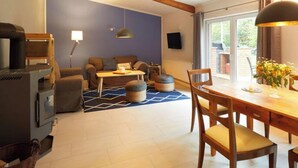 A cozy living room with a fireplace, a dining area with a table and chairs, and a large window providing natural light. - Holiday Apartment Tannenhof Bornholdt (Lutzhorn)