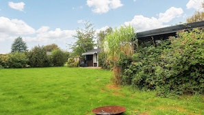 A grassy backyard with a metal bowl, a small shed, and dense shrubbery. - 4 Person Holiday Home in Frorup (Frørup)