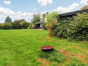 A grassy backyard with a metal bowl, a small shed, and dense shrubbery.