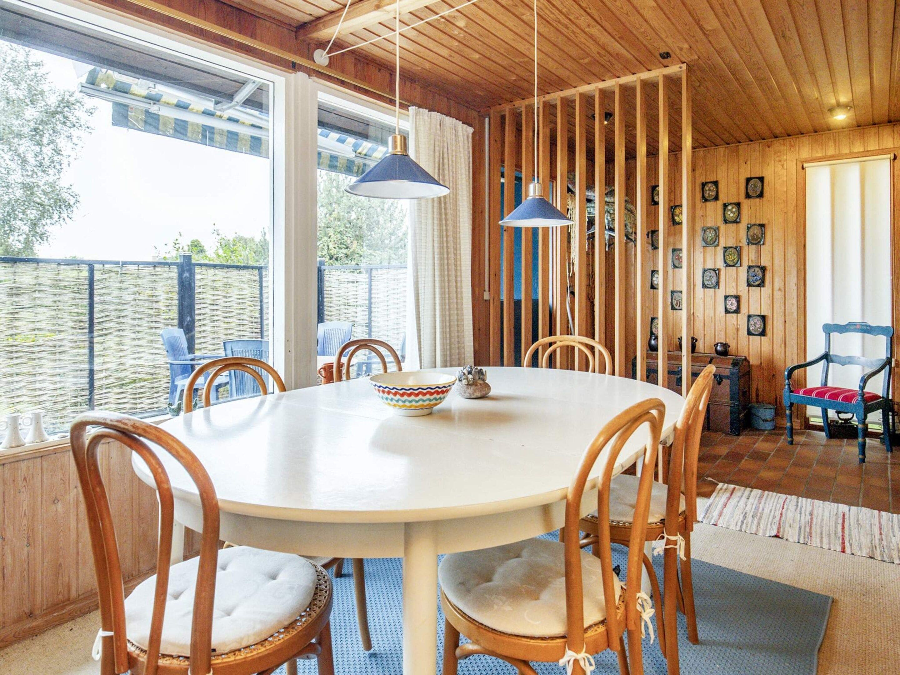 A round dining table with chairs, a hanging light fixture, and a view of the outside.