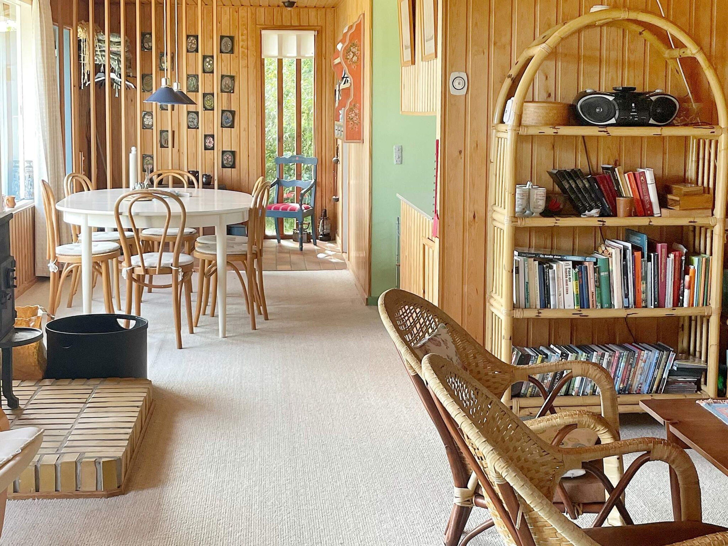Een gezellige kamer met een ronde eettafel, stoelen, een boekenkast en een rieten stoel.