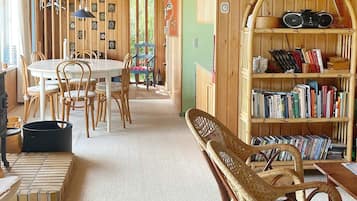 Een gezellige kamer met een ronde eettafel, stoelen, een boekenkast en een rieten stoel.