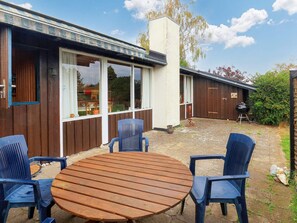 Un patio con una mesa de madera y sillas azules, una parrilla y una valla de madera.
