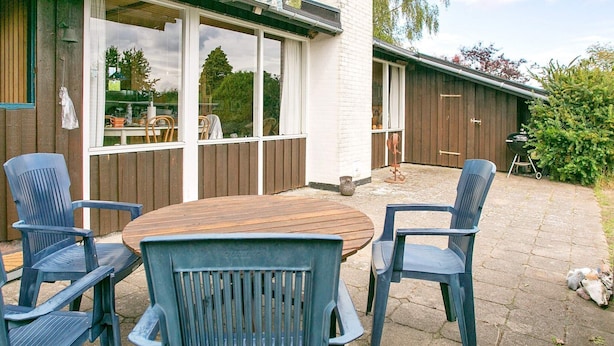 A patio area with a round wooden table and four blue chairs. - 4 Person Holiday Home in Frorup (Frørup)