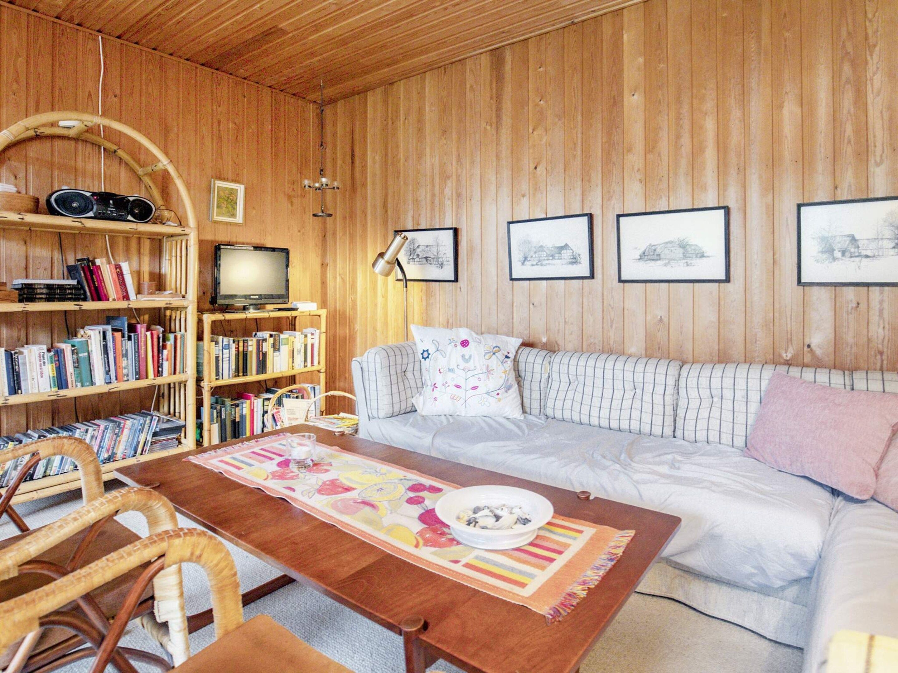 Een gezellige woonkamer met een houten wand, een bank, een salontafel, een boekenkast en een televisie.