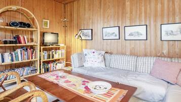 Een gezellige woonkamer met een houten wand, een bank, een salontafel, een boekenkast en een televisie.