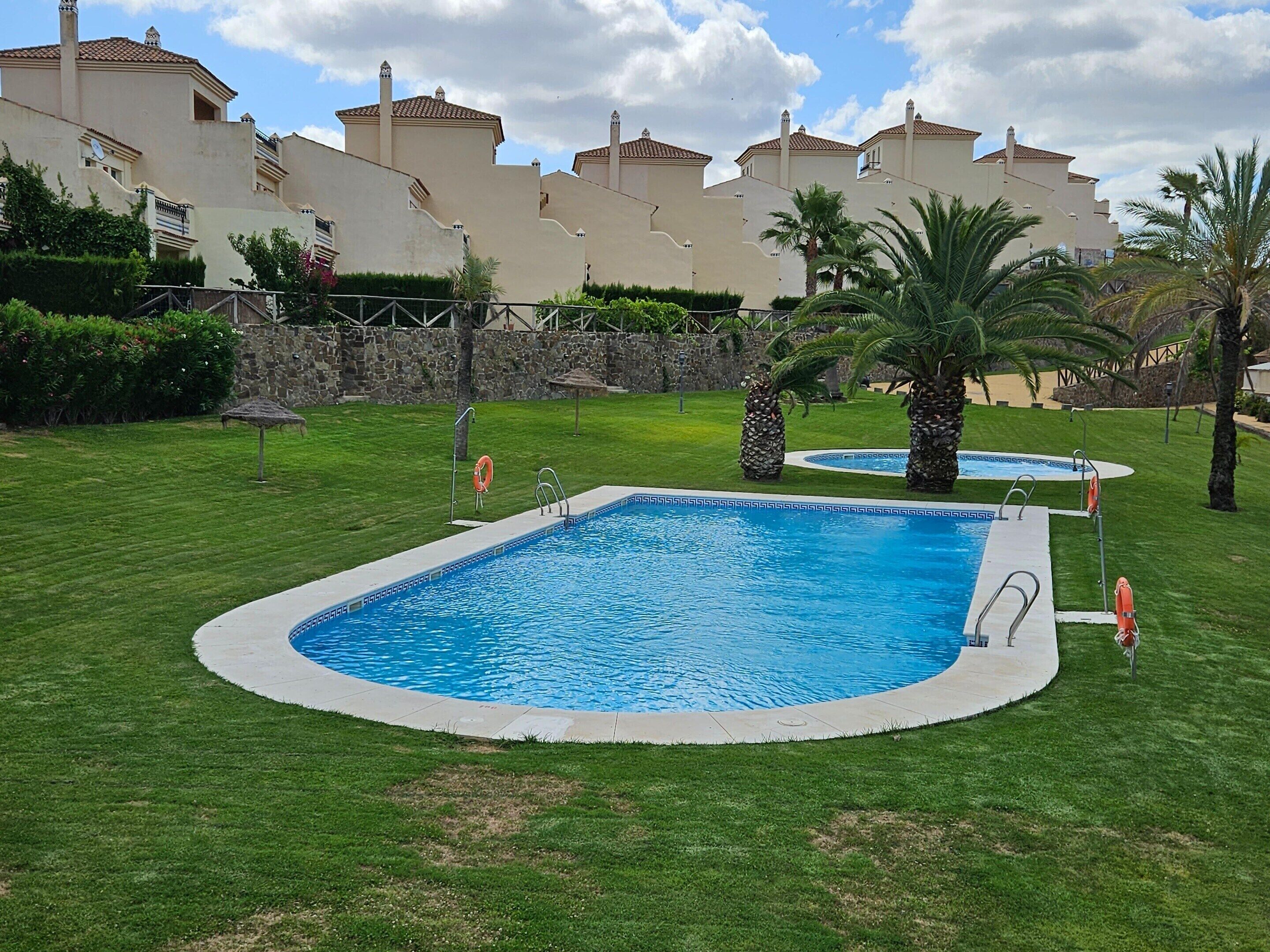 Une piscine entourée d’une pelouse, de palmiers et d’un mur en pierre.