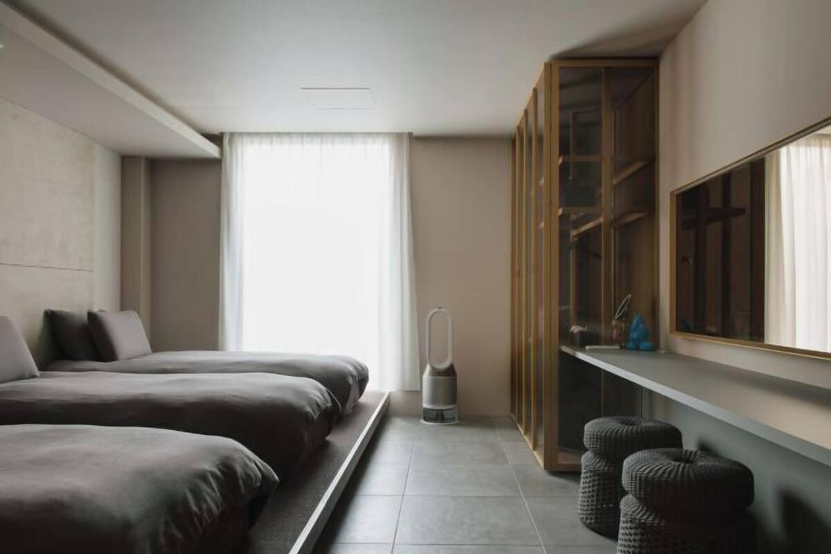 Una habitación de hotel moderna con dos camas, un ventanal grande, un armario empotrado y una mesita de noche.
