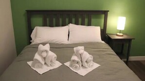 Een hotelkamer met een groene muur, een houten hoofdeinde, een bed met witte lakens en een nachtkastje met een lamp.