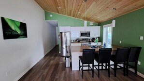 Een moderne keuken met witte kasten, roestvrijstalen apparatuur en een eethoek met een houten tafel en zwarte stoelen.
