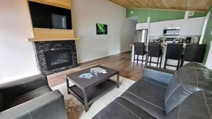 Een moderne woonkamer met een open haard, een bank, een salontafel en een keuken op de achtergrond.